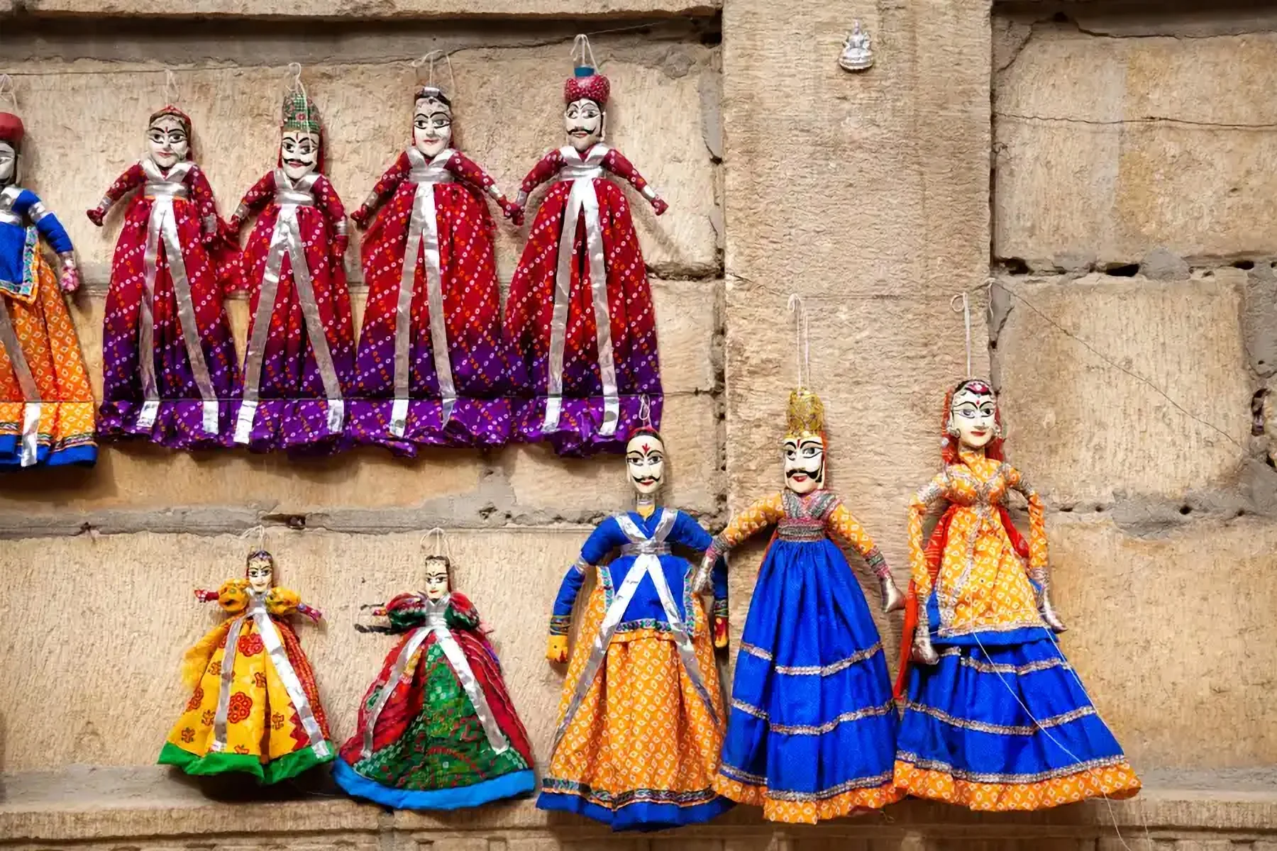 Des marionnettes traditionnelles suspendues à un mur de pierre