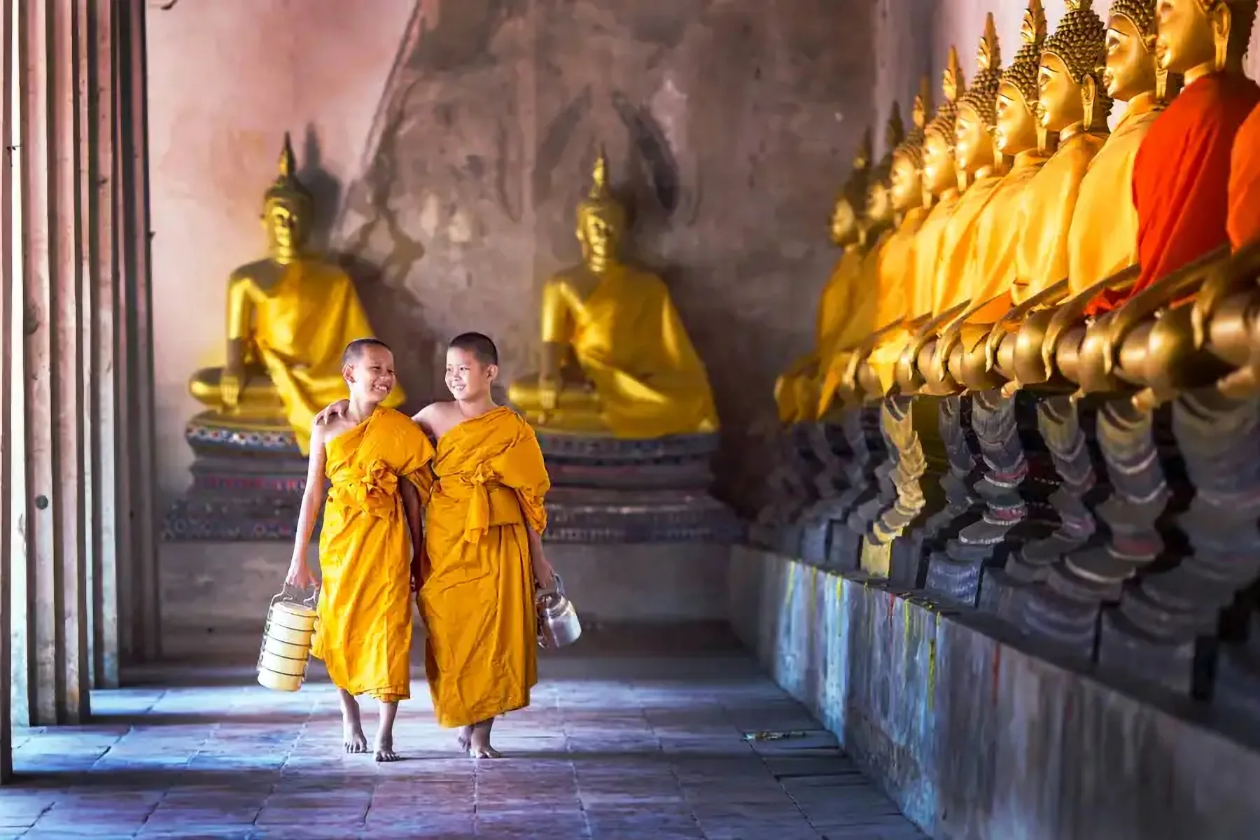 Deux moines en robe safran devant des statues de Bouddha dorées